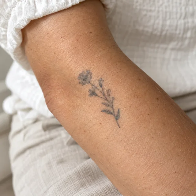 Pequena tatuagem botânica azul-escura desbotada na pele de um antebraço